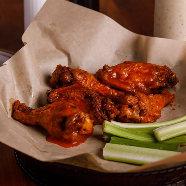 Spicy buffalo chicken wings with celery sticks in a basket lined with parchment paper.