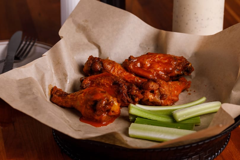 Spicy buffalo chicken wings with celery sticks in a basket lined with parchment paper.