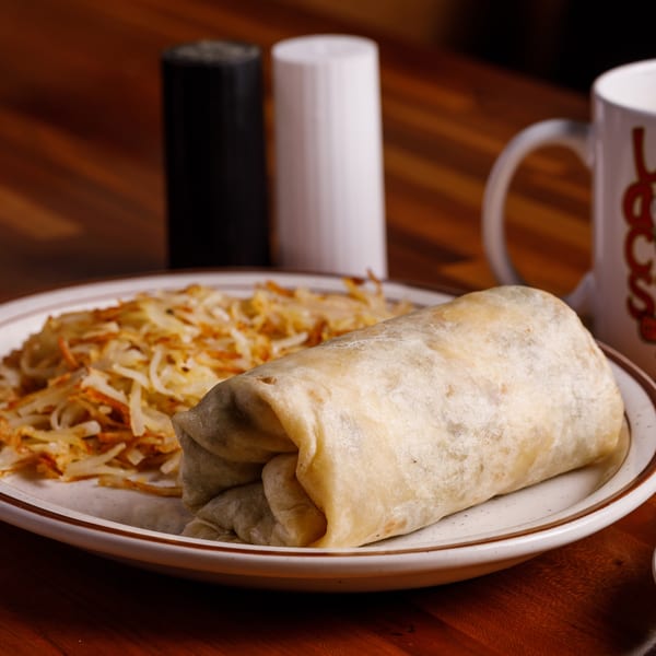 Breakfast burrito and hash browns on a plate with hot sauce, salt, pepper, and coffee.