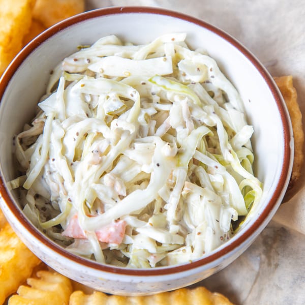 A bowl of creamy coleslaw with mustard seeds, next to golden crinkle-cut fries.