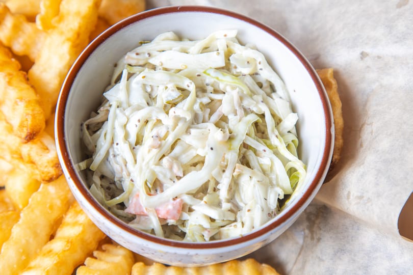 A bowl of creamy coleslaw with mustard seeds, next to golden crinkle-cut fries.
