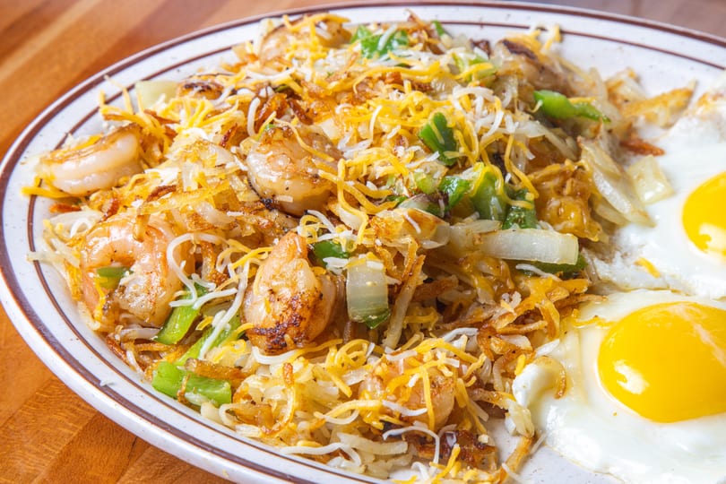 Shrimp and hash browns with green peppers, onions, shredded cheese, and two fried eggs.