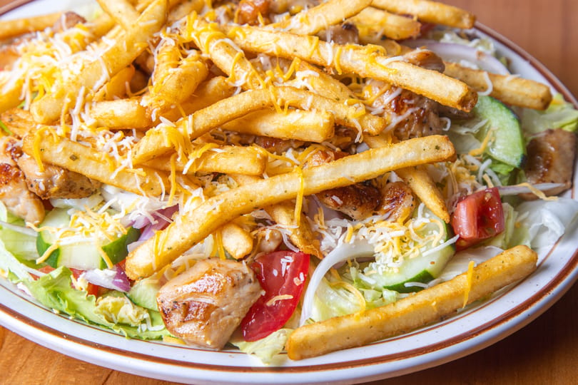 Chicken salad topped with french fries and shredded cheese on a white plate.