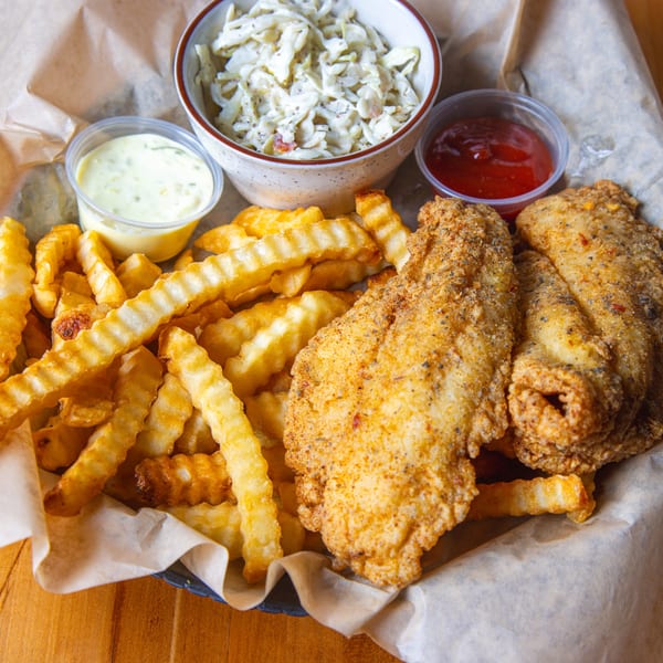 Fried fish and crinkle-cut fries with coleslaw, tartar sauce, and ketchup in a basket.