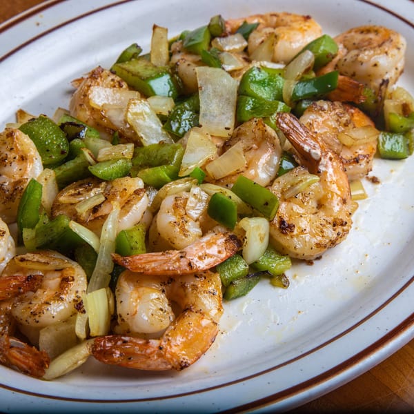 Sautéed shrimp with green bell peppers and onions on a white oval plate with brown trim.