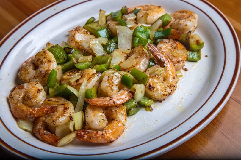 Sautéed shrimp with green bell peppers and onions on a white oval plate with brown trim.