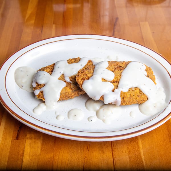 Two crispy fried chicken cutlets covered in creamy white gravy on a white plate.