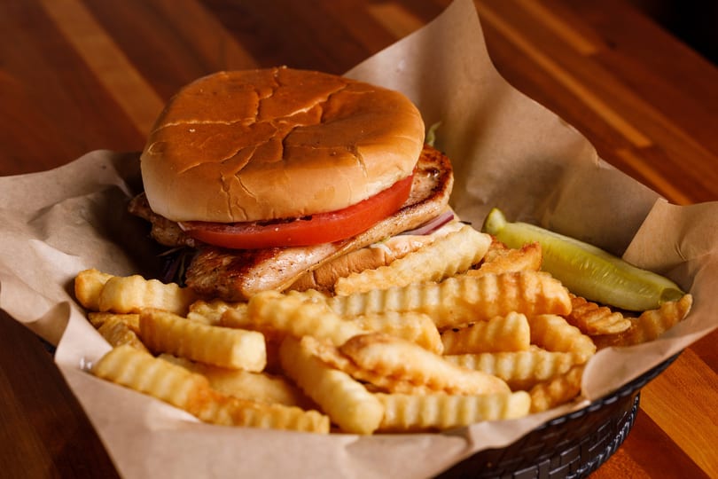 Grilled chicken sandwich with tomato, onion, and lettuce, served with crinkle-cut fries and a pickle.