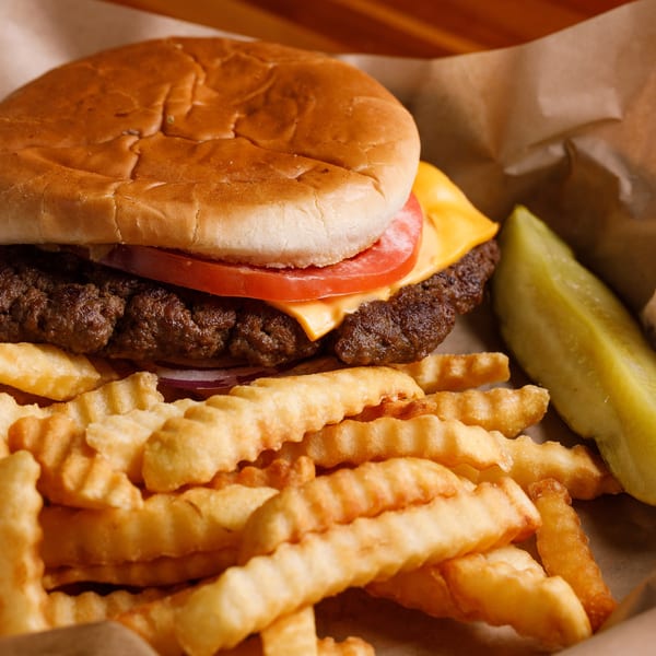 Cheeseburger with tomato, onion, crinkle-cut fries, and a pickle spear in a paper-lined basket.