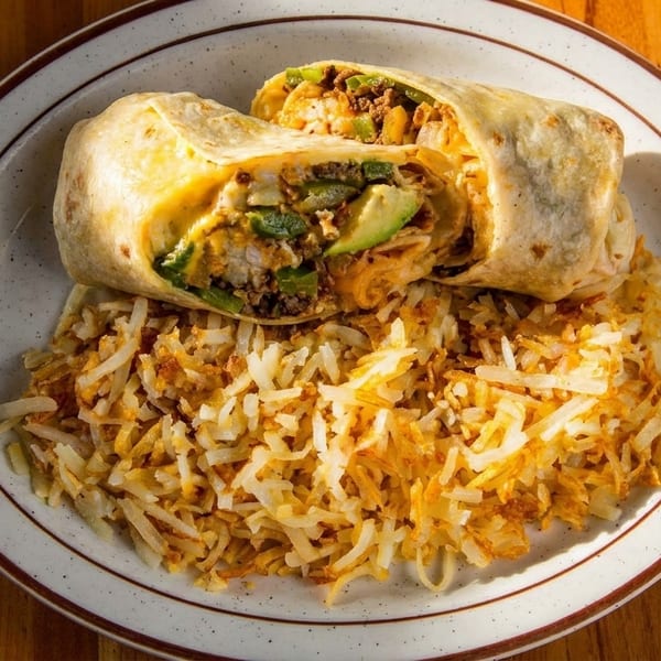 A breakfast burrito, cut in half to show its fillings, served with a side of hash browns.