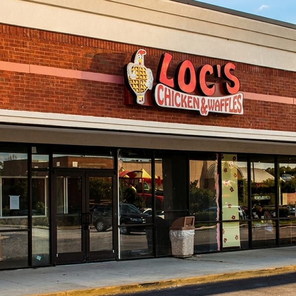 Exterior of Loc's Chicken & Waffles restaurant with a brick facade and large glass windows.