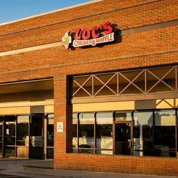 Exterior of Loc's Chicken & Waffle restaurant, a brick building with large windows and a red sign.